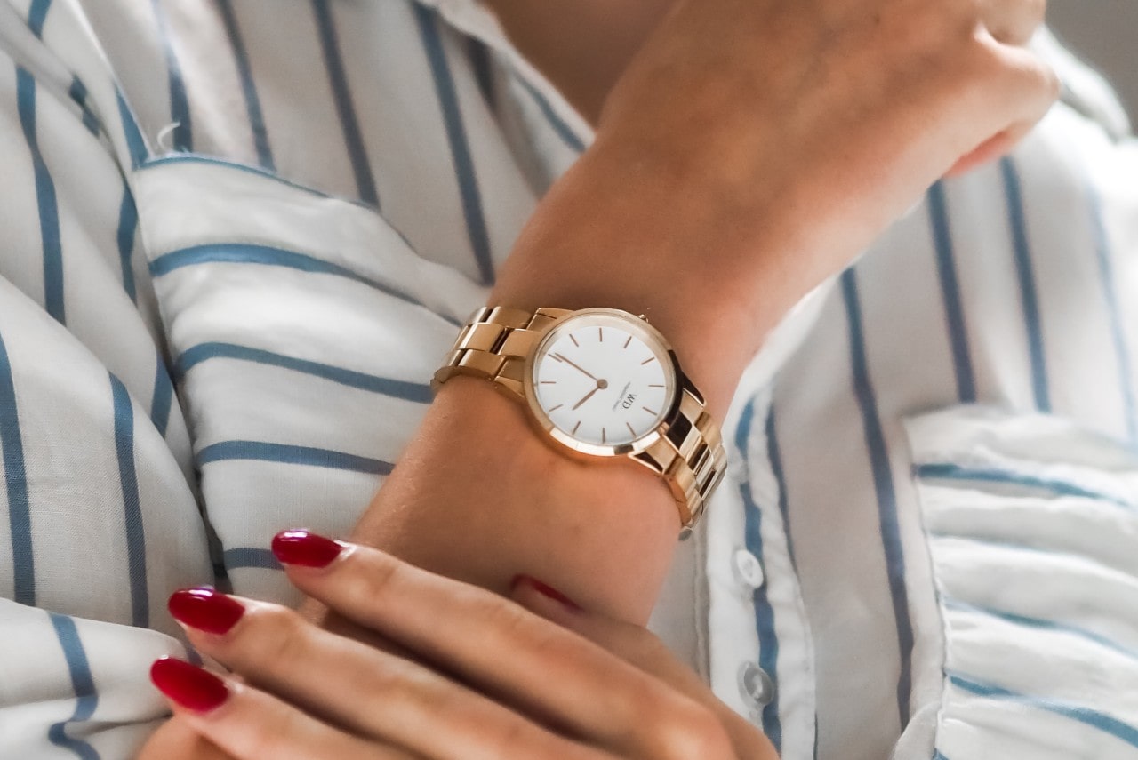 Close up of a woman wearing a striped shirt with a gold watch on her wrist and red fingernails from other hand resting below the watch