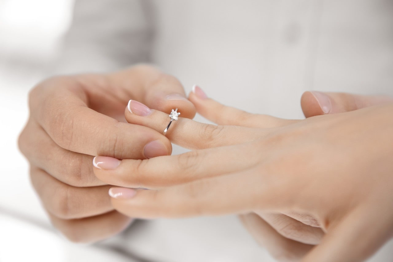 A man putting an engagement ring on a woman's finger with a French manicure