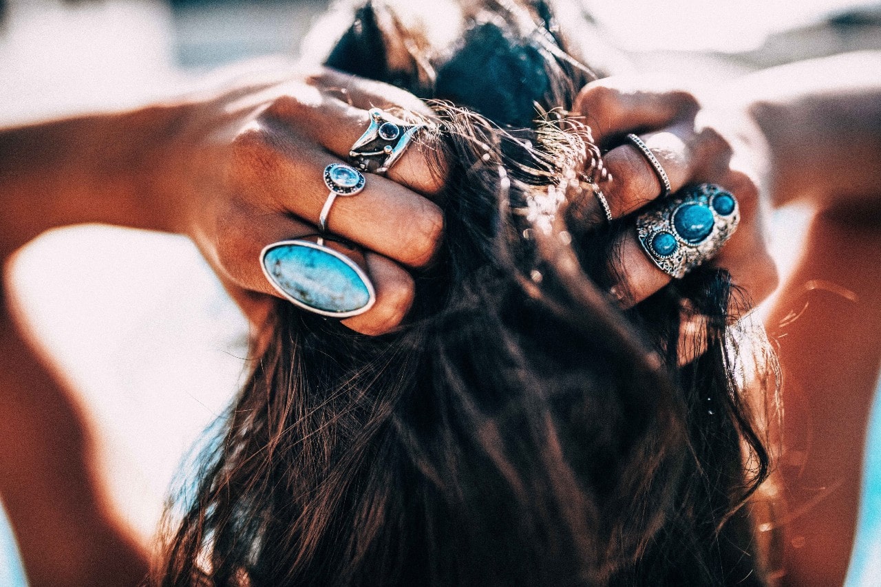 A woman wearing multiple sterling silver and turquoise fashion rings running her hands through her hair