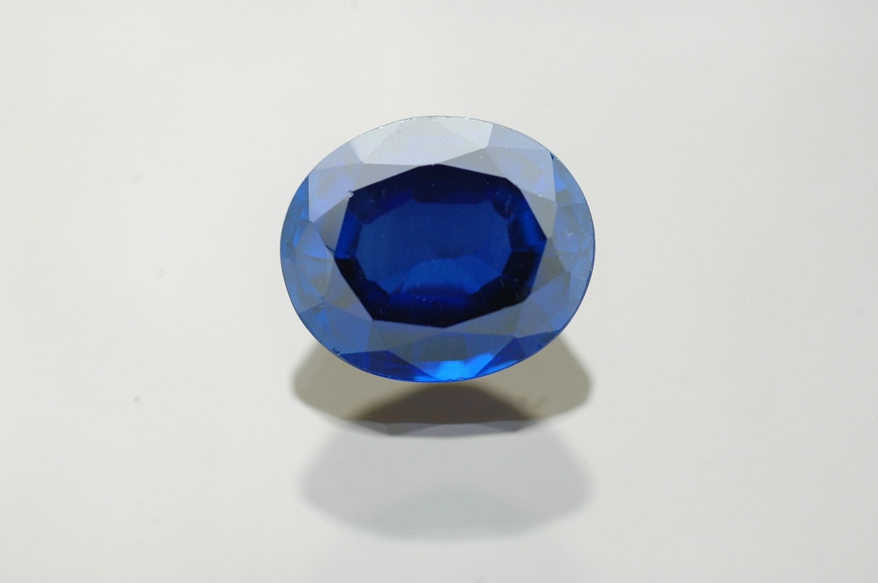 An oval cut sapphire sitting on a plain white surface with a white background