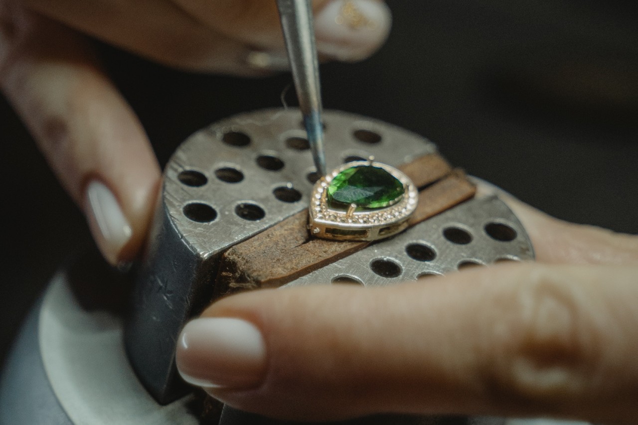 A gold ring being shaped, featuring an emerald center stone