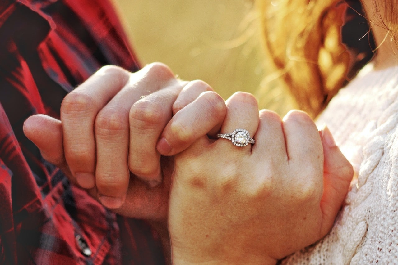 A couple intertwining their pinkies, the woman wearing a silver diamond engagement ring