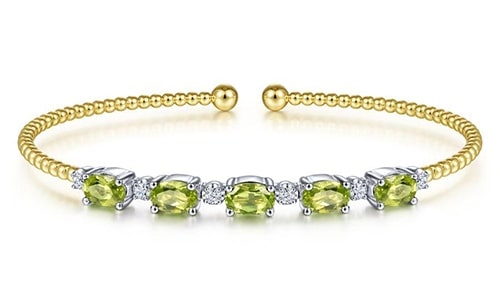A gold cuff bracelet features peridot and diamonds